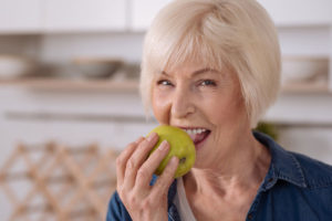 woman with dental implants eating an apple.